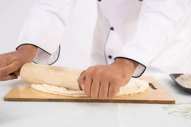 A Saudi chef preparing ingredients for making bread and breakfast, preparing and baking delicious baked goods and pastries, a close-up portrait of an Emirati Gulf Arab man wearing work clothes rolling out dough using a rolling pin, white background