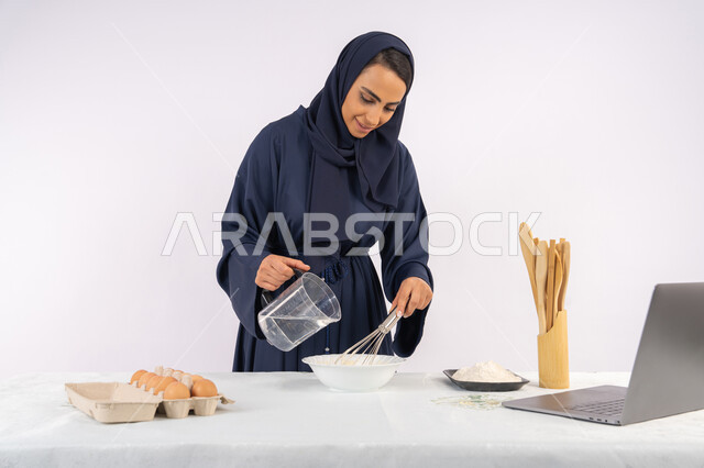 مشاركة الوصفة عبر المواقع باستخدام الحاسوب المحمول، إعداد المخبوزات والمعجنات الشهية، بورتريه مقرب لامرأة عربية خليجية اماراتية محجبة تقوم بخفق المكونات مع الدقيق الابيض لتحضير الطعام، ربة منزل سعودية تقوم بتجهيز المكونات لصناعة الخبز والفطور، خلفية بيضاء