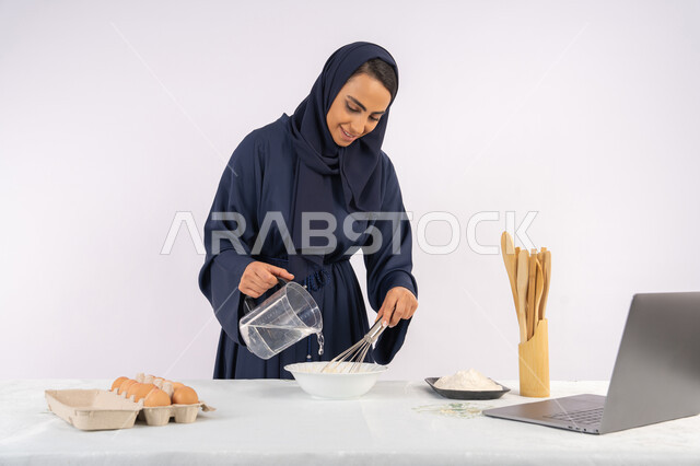 نشر الوصفة عبر المواقع باستخدام الحاسوب المحمول، إعداد المخبوزات والمعجنات الشهية، بورتريه مقرب لامرأة عربية خليجية اماراتية محجبة تقوم بخفق المكونات مع الدقيق الابيض لتحضير الطعام، ربة منزل سعودية تقوم بتجهيز المكونات لصناعة الخبز والفطور، خلفية بيضاء