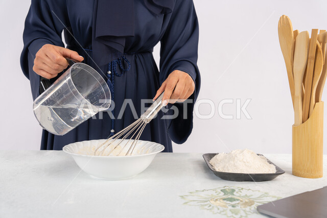 إعداد المخبوزات والمعجنات الشهية، بورتريه مقرب لامرأة عربية خليجية اماراتية محجبة تقوم بخفق المكونات مع الدقيق الابيض لتحضير الطعام، ربة منزل سعودية تقوم بتجهيز المكونات لصناعة الخبز والفطور، خلفية بيضاء