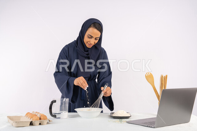 نشر الوصفة عبر المواقع باستخدام الحاسوب المحمول، إعداد المخبوزات والمعجنات الشهية، بورتريه مقرب لامرأة عربية خليجية اماراتية محجبة تقوم بخفق المكونات مع الدقيق الابيض لتحضير الطعام، ربة منزل سعودية تقوم بتجهيز المكونات لصناعة الخبز والفطور، خلفية بيضاء
