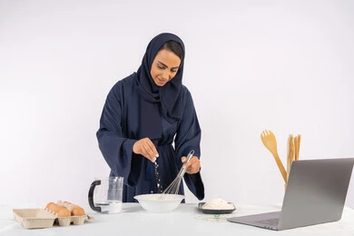 نشر الوصفة عبر المواقع باستخدام الحاسوب المحمول، إعداد المخبوزات والمعجنات الشهية، بورتريه مقرب لامرأة عربية خليجية اماراتية محجبة تقوم بخفق المكونات مع الدقيق الابيض لتحضير الطعام، ربة منزل سعودية تقوم بتجهيز المكونات لصناعة الخبز والفطور، خلفية بيضاء