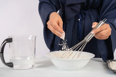 طهي المخبوزات والمعجنات الشهية، بورتريه مقرب لامرأة عربية خليجية اماراتية محجبة تقوم بخفق المكونات مع الدقيق الابيض لتحضير الطعام، ربة منزل سعودية تقوم بتجهيز المكونات لصناعة الخبز والفطور، خلفية بيضاء