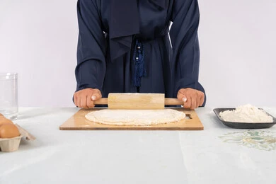 A Saudi housewie preparing ingredients for making bread and breakfast, preparing and baking delicious baked goods and pastries, a close-up portrait of a veiled Emirati Gulf Arab woman rolling out dough using a rolling pin, white background