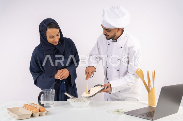 تصوير وعرض الطبخ عبر جهاز الحاسوب المحمول، وضع المقادير والمكونات المعيارية، ربة منزل سعودية تقوم بتعلم صناعة الخبز والمعجنات،  دورة تحضير وإعداد المخبوزات الشهية، بورتريه لشيف عربي خليجي اماراتي يقوم بتدريب إمرأة على اساسيات العمل في المطبخ، خلفية بيضاء
