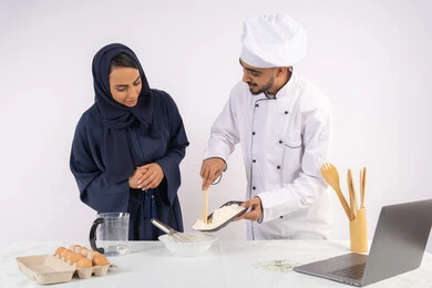 Photographing and displaying cooking on a laptop, setting the standard quantities and ingredients, a Saudi housewife learning how to make bread and pastries, a course on preparing and making delicious baked goods, a portrait of an Arab Gulf Emirati chef training a woman on the basics of working in the kitchen, white background