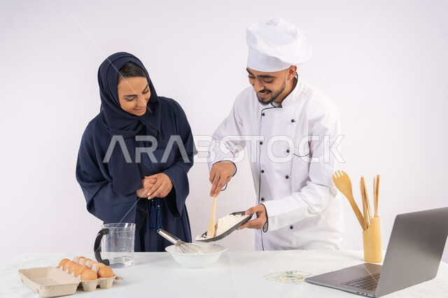 Photographing and displaying cooking on a laptop, setting the standard quantities and ingredients, a Saudi housewife learning how to make bread and pastries, a course on preparing and making delicious baked goods, a portrait of an Arab Gulf Emirati chef training a woman on the basics of working in the kitchen, white background