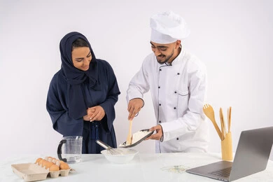 تصوير وعرض الطبخ عبر جهاز الحاسوب المحمول، وضع المقادير والمكونات المعيارية، ربة منزل سعودية تقوم بتعلم صناعة الخبز والمعجنات،  دورة تحضير وإعداد المخبوزات الشهية، بورتريه لشيف عربي خليجي اماراتي يقوم بتدريب إمرأة على اساسيات العمل في المطبخ، خلفية بيضاء