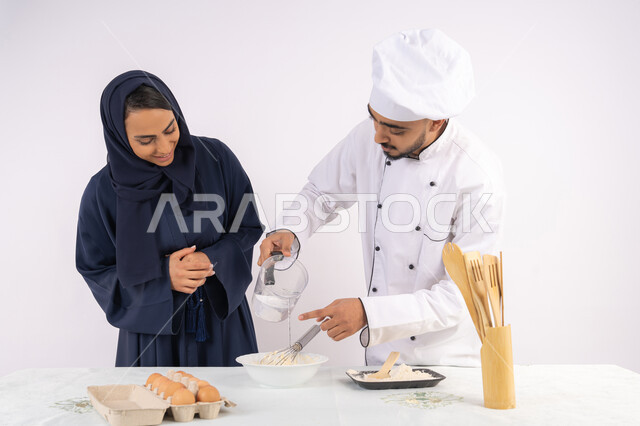 وضع المقادير والمكونات المعيارية، ربة منزل سعودية تقوم بتعلم صناعة الخبز والمعجنات،  دورة تحضير وإعداد المخبوزات الشهية، بورتريه لشيف عربي خليجي اماراتي يقوم بتدريب إمرأة على اساسيات العمل في المطبخ، خلفية بيضاء