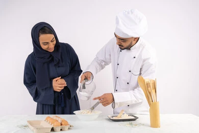 Setting standard quantities and ingredients, a Saudi housewife learning how to make bread and pastries, a course on preparing and making delicious baked goods, a portrait of an Arab Gulf Emirati chef training a woman on the basics of working in the kitchen, white background