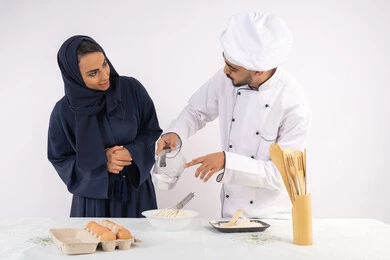 Training on standard quantities and ingredients, a Saudi housewife learning how to make bread and pastries, a course on preparing and making delicious baked goods, a portrait of an Arab Gulf Emirati chef training a woman on the basics of working in the kitchen, white background
