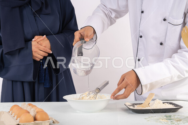 وضع المقادير والمكونات المعيارية، ربة منزل سعودية تقوم بتعلم صناعة الخبز والمعجنات،  دورة تحضير وإعداد المخبوزات الشهية، بورتريه لشيف عربي خليجي اماراتي يقوم بتدريب إمرأة على اساسيات العمل في المطبخ، خلفية بيضاء