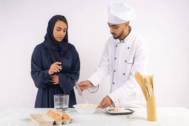 المقادير والمكونات المعيارية، ربة منزل سعودية تقوم بتعلم صناعة الخبز والمعجنات،  دورة تحضير وإعداد المخبوزات الشهية، بورتريه لشيف عربي خليجي اماراتي يقوم بتدريب إمرأة على اساسيات العمل في المطبخ، خلفية بيضاء