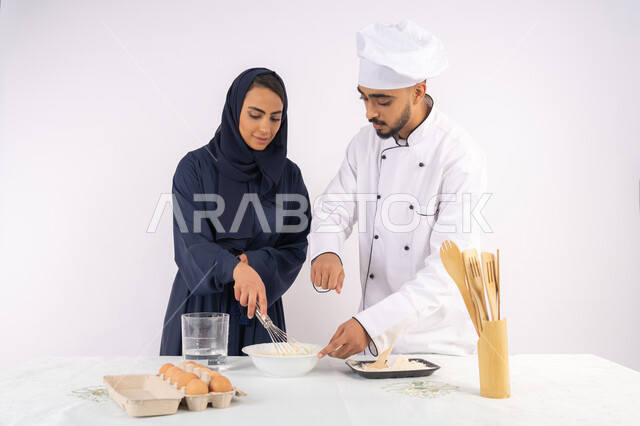 التدرب على المقادير والمكونات المعيارية، ربة منزل سعودية تقوم بتعلم صناعة الخبز والمعجنات،  دورة تحضير وإعداد المخبوزات الشهية، بورتريه لشيف عربي خليجي اماراتي يقوم بتدريب إمرأة على اساسيات العمل في المطبخ، خلفية بيضاء