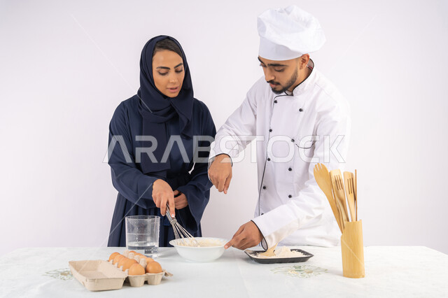 وضع المقادير والمكونات المعيارية، ربة منزل سعودية تقوم بتعلم صناعة الخبز والمعجنات،  دورة تحضير وإعداد المخبوزات الشهية، بورتريه لشيف عربي خليجي اماراتي يقوم بتدريب إمرأة على اساسيات العمل في المطبخ، خلفية بيضاء
