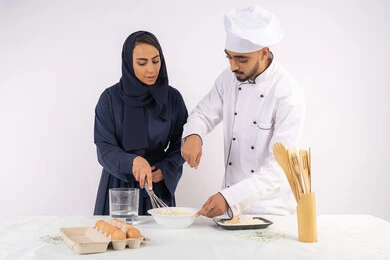وضع المقادير والمكونات المعيارية، ربة منزل سعودية تقوم بتعلم صناعة الخبز والمعجنات،  دورة تحضير وإعداد المخبوزات الشهية، بورتريه لشيف عربي خليجي اماراتي يقوم بتدريب إمرأة على اساسيات العمل في المطبخ، خلفية بيضاء