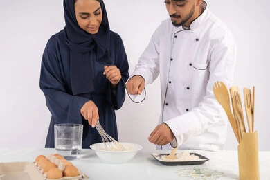 وضع المقادير والمكونات المعيارية، ربة منزل سعودية تقوم بتعلم صناعة الخبز والمعجنات،  دورة تحضير وإعداد المخبوزات الشهية، بورتريه لشيف عربي خليجي اماراتي يقوم بتدريب إمرأة على اساسيات العمل في المطبخ، خلفية بيضاء