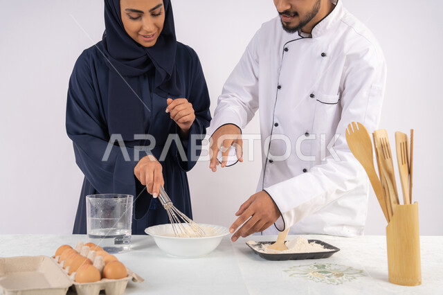 وضع المقادير والمكونات المعيارية، ربة منزل سعودية تقوم بتعلم صناعة الخبز والمعجنات،  دورة تحضير وإعداد المخبوزات الشهية، بورتريه لشيف عربي خليجي اماراتي يقوم بتدريب إمرأة على اساسيات العمل في المطبخ، خلفية بيضاء