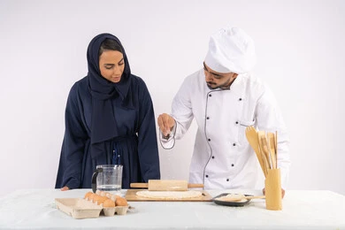 A course in preparing and making delicious baked goods, a portrait of an Emirati Gulf Arab chef training a woman on the basics of working in the kitchen, rolling out dough using a rolling pin, a Saudi housewife learning how to make bread and pastries, white background