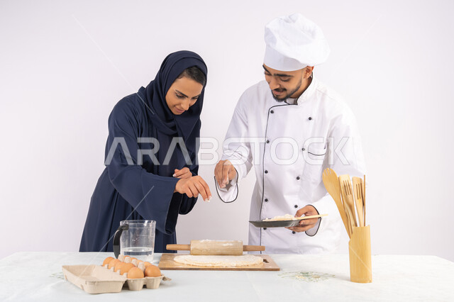 دورة تحضير وإعداد المخبوزات الشهية، بورتريه لشيف عربي خليجي اماراتي يقوم بتدريب إمرأة على اساسيات العمل في المطبخ، فرد العجين باستخدام الشوبك (النشابة)، ربة منزل سعودية تقوم بتعلم صناعة الخبز والمعجنات، خلفية بيضاء