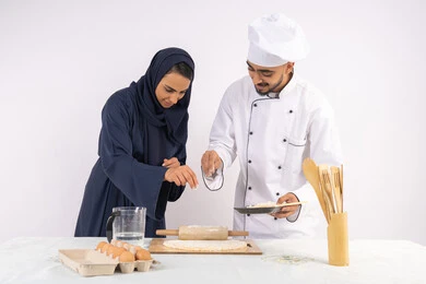 A course in preparing and making delicious baked goods, a portrait of an Emirati Gulf Arab chef training a woman on the basics of working in the kitchen, rolling out dough using a rolling pin, a Saudi housewife learning how to make bread and pastries, white background