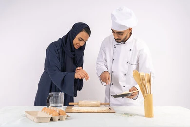 Dough rolling skill using a rolling pin, a Saudi housewife learning how to make bread and pastries, a course on preparing and making delicious baked goods, a portrait of an Emirati Gulf Arab chef training a woman on the basics of working in the kitchen, white background