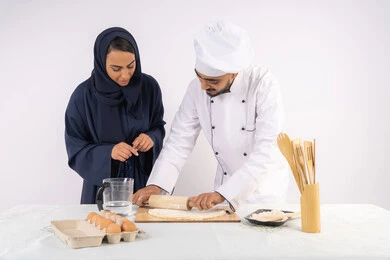 دورة تحضير وإعداد المخبوزات الشهية، بورتريه لشيف عربي خليجي اماراتي يقوم بتدريب إمرأة على اساسيات العمل في المطبخ، فرد العجين باستخدام الشوبك (النشابة)، ربة منزل سعودية تقوم بتعلم صناعة الخبز والمعجنات، خلفية بيضاء