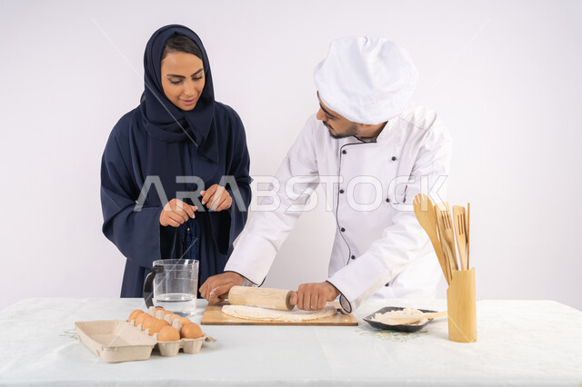 ربة منزل سعودية تقوم بتعلم صناعة الخبز والمعجنات،  دورة تحضير وإعداد المخبوزات الشهية، بورتريه لشيف عربي خليجي اماراتي يقوم بتدريب إمرأة على اساسيات العمل في المطبخ، مهارة فرد العجين باستخدام الشوبك (النشابة)، خلفية بيضاء