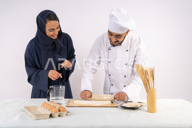 مهارة فرد العجين باستخدام الشوبك (النشابة)، ربة منزل سعودية تقوم بتعلم صناعة الخبز والمعجنات،  دورة تحضير وإعداد المخبوزات الشهية، بورتريه لشيف عربي خليجي اماراتي يقوم بتدريب إمرأة على اساسيات العمل في المطبخ، خلفية بيضاء