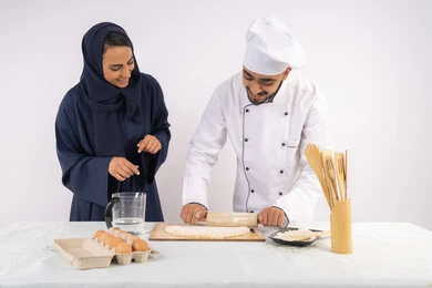 Dough rolling skill using a rolling pin, a Saudi housewife learning how to make bread and pastries, a course on preparing and making delicious baked goods, a portrait of an Emirati Gulf Arab chef training a woman on the basics of working in the kitchen, white background