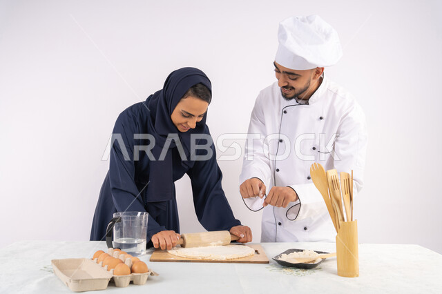 طباخة سعودية تقوم بتعلم صناعة الخبز والمعجنات،  دورة تحضير وإعداد المخبوزات الشهية، بورتريه لشيف عربي خليجي اماراتي يقوم بتدريب إمرأة على اساسيات العمل في المطبخ، مهارة فرد العجين باستخدام الشوبك (النشابة)، خلفية بيضاء