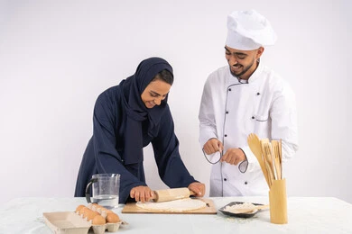 Dough rolling skill using a rolling pin, a Saudi housewife learning how to make bread and pastries, a course on preparing and making delicious baked goods, a portrait of an Emirati Gulf Arab chef training a woman on the basics of working in the kitchen, white background