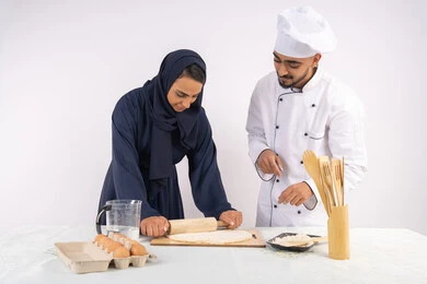 A course in preparing and making delicious baked goods, a portrait of an Emirati Gulf Arab chef training a woman on the basics of working in the kitchen, rolling out dough using a rolling pin, a Saudi housewife learning how to make bread and pastries, white background