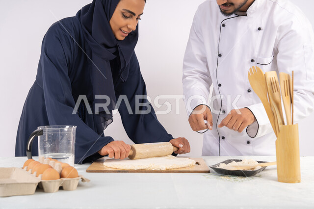 طباخة سعودية تقوم بتعلم صناعة الخبز والمعجنات،  دورة تحضير وإعداد المخبوزات الشهية، بورتريه لشيف عربي خليجي اماراتي يقوم بتدريب إمرأة على اساسيات العمل في المطبخ، مهارة فرد العجين باستخدام الشوبك (النشابة)، خلفية بيضاء