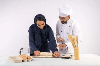 دورة تحضير وإعداد المخبوزات الشهية، بورتريه لشيف عربي خليجي اماراتي يقوم بتدريب إمرأة على اساسيات العمل في المطبخ، فرد العجين باستخدام الشوبك (النشابة)، ربة منزل سعودية تقوم بتعلم صناعة الخبز والمعجنات، خلفية بيضاء