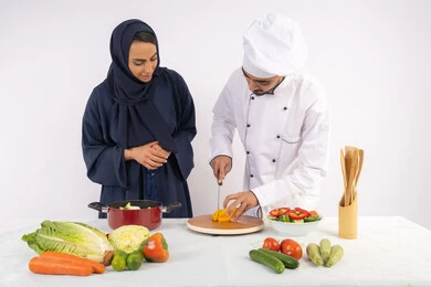 Professional vegetable cutting, Saudi housewife learning to cook and prepare dishes, course on preparing recipes for salads and delicious healthy meals, portrait of an Arab Gulf Emirati chef training a woman on the basics of working in the kitchn, white background