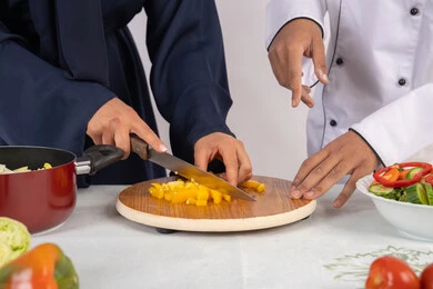 A course on preparing recipes for delicious salads and healthy meals. A close-up portrait of an Emirati Gulf Arab chef training a woman on the basics of working in the kitchen. Learning the skill of cutting vegetables. A Saudi housewife learning to cook and prepare dishes. White background.