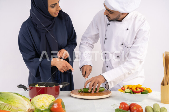 A course on preparing delicious, healthy salad and meal recipes. A portrait of an Emirati Gulf Arab chef training a woman on the basics of working in the kitchen. Learning the skill of cutting vegetables. A Saudi housewife learning to cook and prepare dishes. White background.