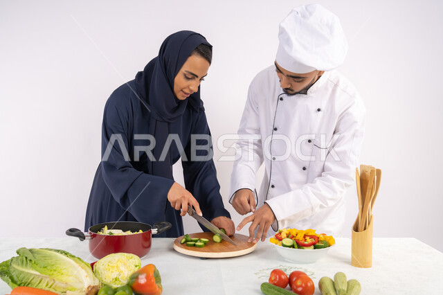 فن تقطيع الخضراوات، ربة منزل سعودية تقوم بتعلم الطهي وإعداد الأطباق، دورة تحضير وصفات السلطات والوجبات الصحية الشهية، بورتريه لشيف عربي خليجي اماراتي يقوم بتدريب إمرأة على اساسيات العمل في المطبخ، خلفية بيضاء