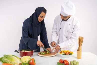Professional vegetable cutting, Saudi housewife learning to cook and prepare dishes, course on preparing recipes for salads and delicious healthy meals, portrait of an Arab Gulf Emirati chef training a woman on the basics of working in the kitchen, white background