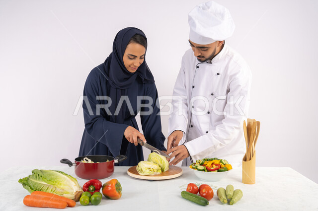 Learning the skill of cutting vegetables, a Saudi housewife learning to cook and prepare dishes, a course in preparing recipes for salads and delicious healthy meals, a portrait of an Arab Gulf Emirati chef training a woman on the basics of working in the kitchen, white background
