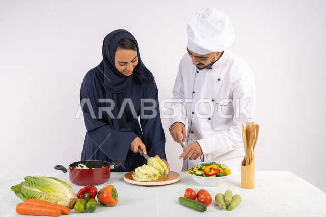 مهارة  تقطيع الخضراوات، ربة منزل سعودية تقوم بتعلم الطهي وإعداد الأطباق، دورة تحضير وصفات السلطات والوجبات الصحية الشهية، بورتريه لشيف عربي خليجي اماراتي يقوم بتدريب إمرأة على اساسيات العمل في المطبخ، خلفية بيضاء