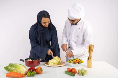 مهارة  تقطيع الخضراوات، ربة منزل سعودية تقوم بتعلم الطهي وإعداد الأطباق، دورة تحضير وصفات السلطات والوجبات الصحية الشهية، بورتريه لشيف عربي خليجي اماراتي يقوم بتدريب إمرأة على اساسيات العمل في المطبخ، خلفية بيضاء