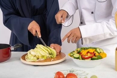 A course on preparing recipes for delicious salads and healthy meals. A close-up portrait of an Emirati Gulf Arab chef training a woman on the basics of working in the kitchen. Learning the skill of cutting vegetables. A Saudi housewife learning to cook and prepare dishes. White background.