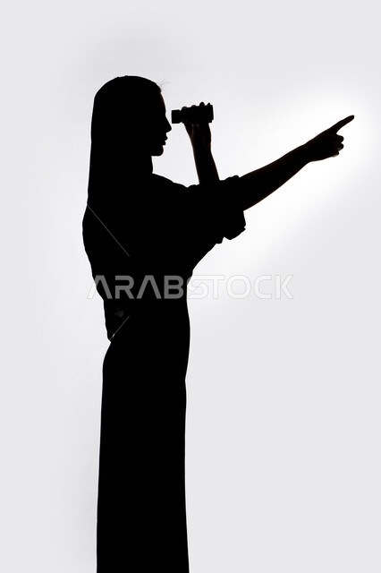 رؤية الاشياء البعيدة و تقريبها, حب الاستكشاف و المغامرة, الاشاره الى شئ بعيد،  صورة ظلية لمراه عربية خليجية اماراتية تحمل بيدها منظار ثنائي العينين و تنظر الى شيء ما بإيماءات السرور والاستمتاع، خلفية بيضاء