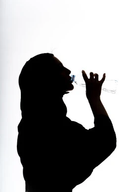 Silhouette of an Arab Gulf Emirati woman drinking water from a plastic bottle, detoxifying the body, maintaining a healthy immune system, importance of drinking pure water to maintain fresh skin, white background