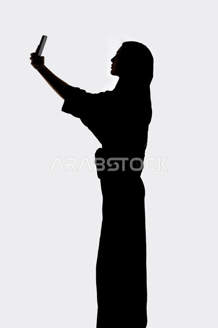 التواصل الإجتماعي ،اجراء مكالمه هاتفيه ، إستخدام اجهزة تقنية حديثة ،التقاط صور سيلفي تذكاريه بإستخدام الهاتف المحمول ، صورة ظلية لمرأة عربية خليجية اماراتيه ، بث مباشر ، خلفية بيضاء