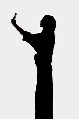 التواصل الإجتماعي ،اجراء مكالمه هاتفيه ، إستخدام اجهزة تقنية حديثة ،التقاط صور سيلفي تذكاريه بإستخدام الهاتف المحمول ، صورة ظلية لمرأة عربية خليجية اماراتيه ، بث مباشر ، خلفية بيضاء