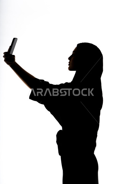 إستخدام اجهزة تقنية حديثة ، التواصل الإجتماعي ،اجراء مكالمه هاتفيه ،التقاط صور سيلفي تذكاريه بإستخدام الهاتف المحمول ، صورة ظلية لمرأة عربية خليجية اماراتيه ، بث مباشر ، خلفية بيضاء