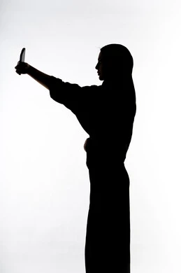 اجراء مكالمه هاتفيه ،التقاط صور سيلفي تذكاريه بإستخدام الهاتف المحمول ، صورة ظلية لمرأة عربية خليجية اماراتيه ، إستخدام اجهزة تقنية حديثة ، التواصل الإجتماعي ، بث مباشر ، خلفية بيضاء